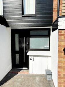 Black cladding and black front door, next to repaired electricity meter cupboard